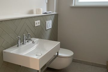 Modernes Badezimmer mit Waschtisch, wandhängendem WC und Herringbone-Fliesen.
