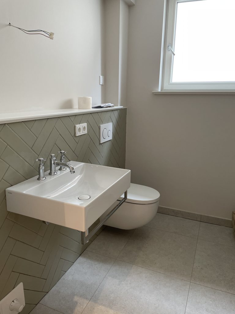 Modernes Badezimmer mit Waschtisch, wandhängendem WC und Herringbone-Fliesen.