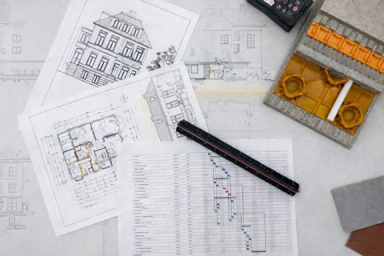 Architekturpläne und Grundrisse auf einem Tisch mit Bleistift, Lineal und einem kleinen Hausmodell.